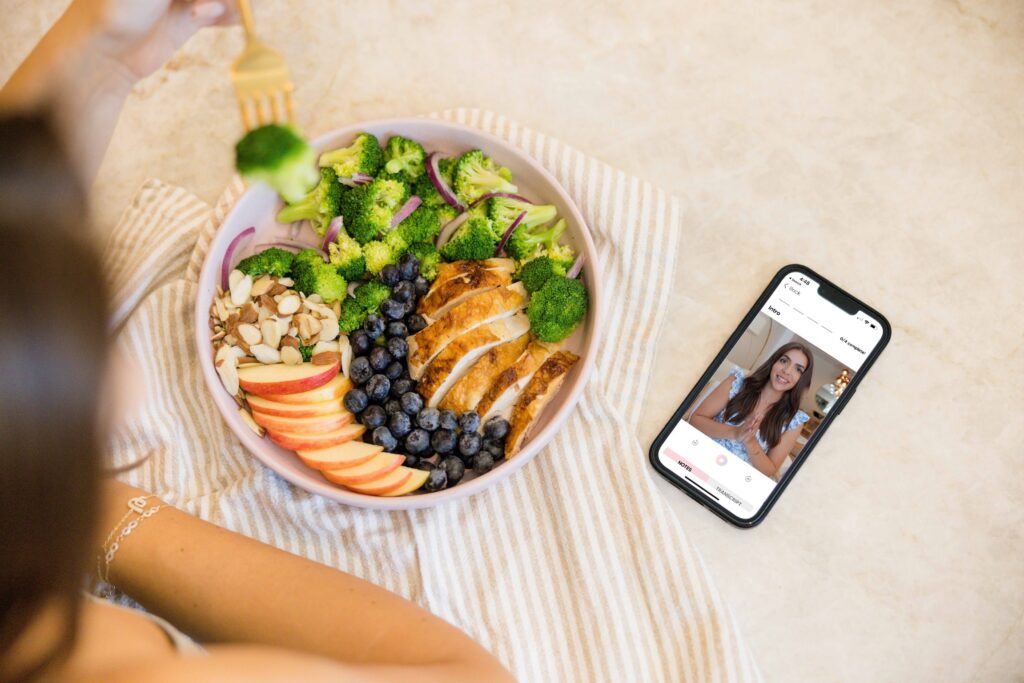 Woman eating a healthy plate at a table with her cell phone in view