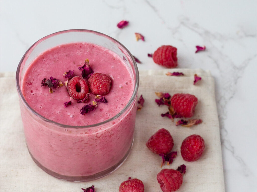 Pink smoothie with raspberry on top in glass cup