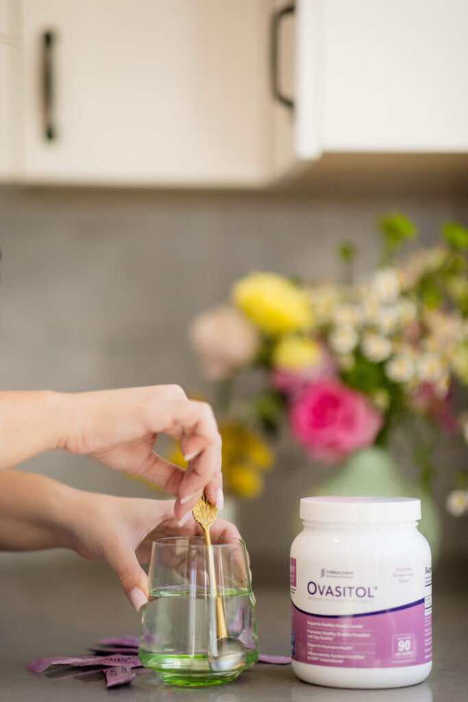 ovasitol woman's hands stirring a spoon in water glass with ovasitol container next to it