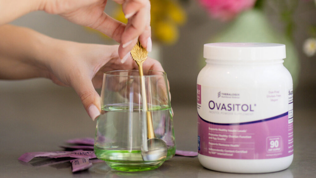 woman's hands stirring a spoon in water glass with ovasitol