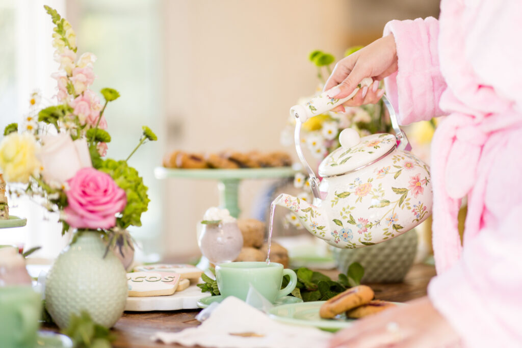 Pouring hot water into a tea cup from a tea pot on a table decorated for a tea party