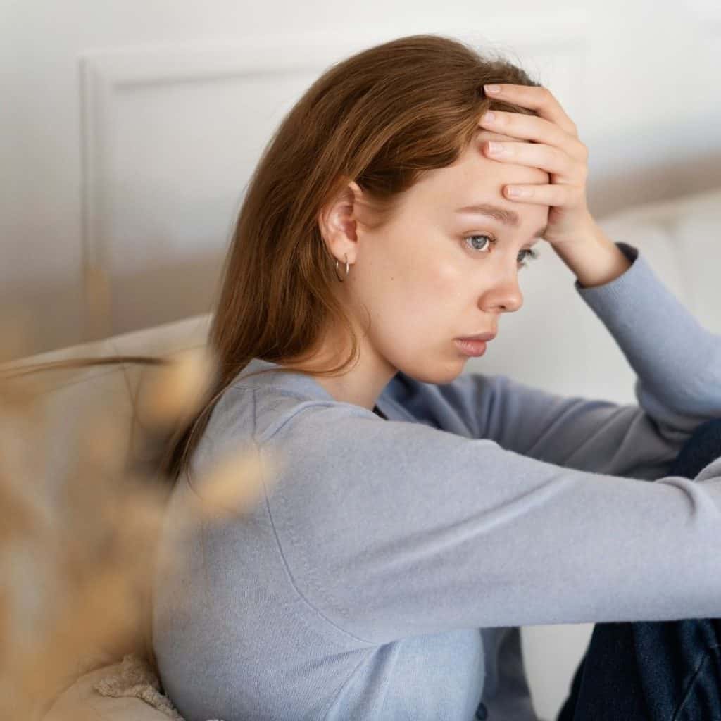 anxious woman Young woman sitting on a couch with a hand on her forehead, looking anxious or deep in thought.
