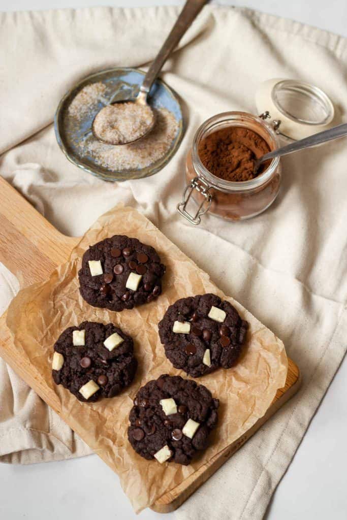 double chocolate cookies on a wooden board with cocoa powder next to them
